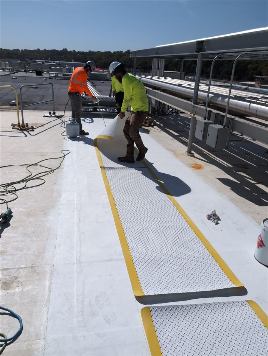 Crew installing a single-ply membrane and walkway pads on a low-slope commercial roof